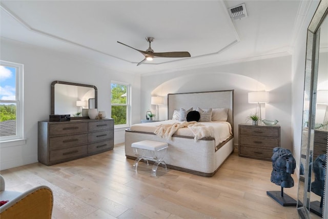 bedroom with ceiling fan, visible vents, light wood-type flooring, a raised ceiling, and ornamental molding