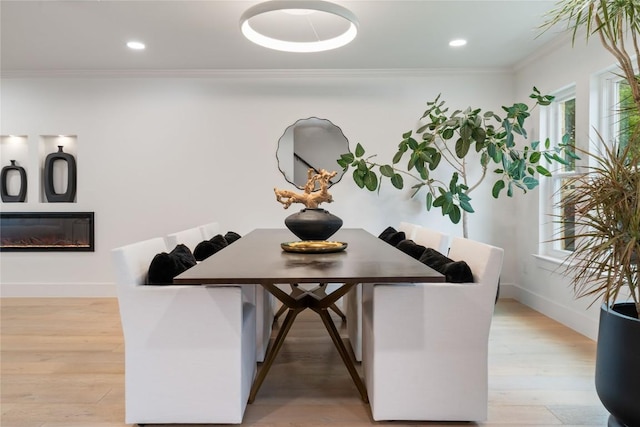 dining room featuring crown molding, baseboards, a glass covered fireplace, and light wood-style floors