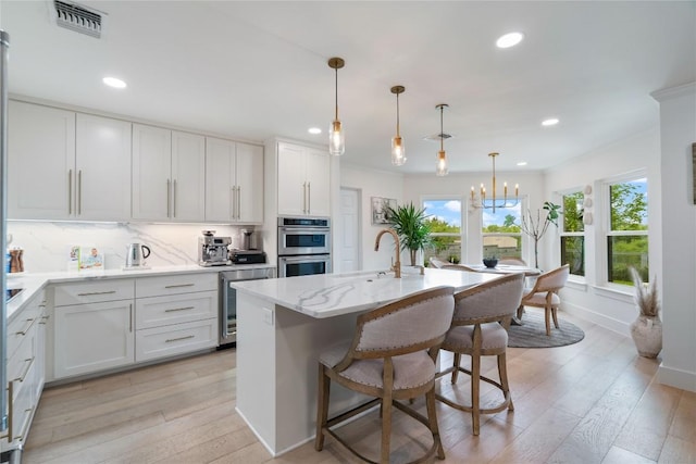 kitchen with a sink, double oven, beverage cooler, light wood-type flooring, and visible vents