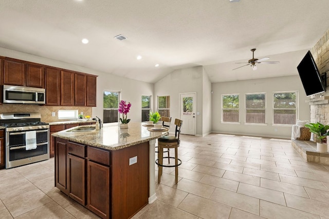 kitchen with a kitchen island with sink, a sink, a kitchen bar, appliances with stainless steel finishes, and open floor plan
