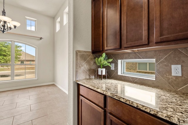 interior space featuring hanging light fixtures, light stone counters, backsplash, baseboards, and a notable chandelier