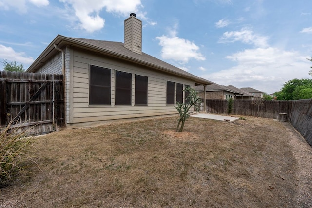 back of property featuring a chimney, a fenced backyard, a patio area, and a lawn