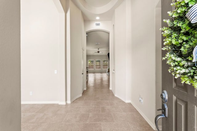 corridor with light tile patterned floors, arched walkways, visible vents, and baseboards