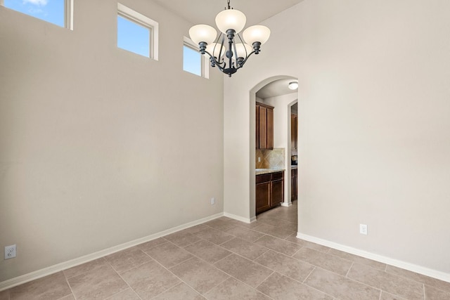 empty room featuring light tile patterned floors, arched walkways, a notable chandelier, and baseboards