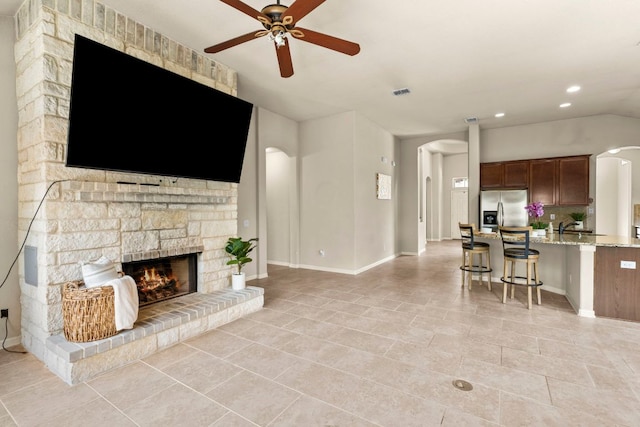 living area with a fireplace, light tile patterned floors, ceiling fan, and arched walkways