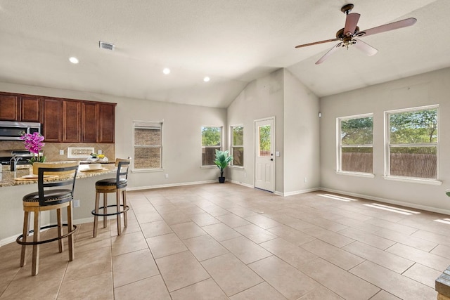 kitchen featuring light stone counters, light tile patterned floors, stainless steel microwave, tasteful backsplash, and open floor plan