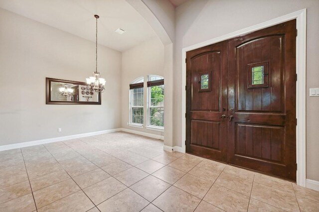 entrance foyer with baseboards, light tile patterned floors, arched walkways, and an inviting chandelier