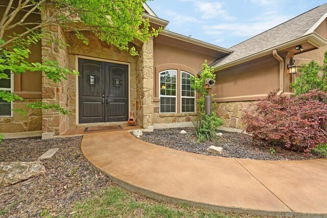 entrance to property with stucco siding, roof with shingles, and stone siding