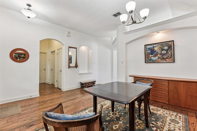dining space featuring an inviting chandelier, visible vents, baseboards, arched walkways, and wood finished floors