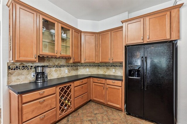 kitchen featuring stone finish floor, decorative backsplash, glass insert cabinets, dark countertops, and black fridge