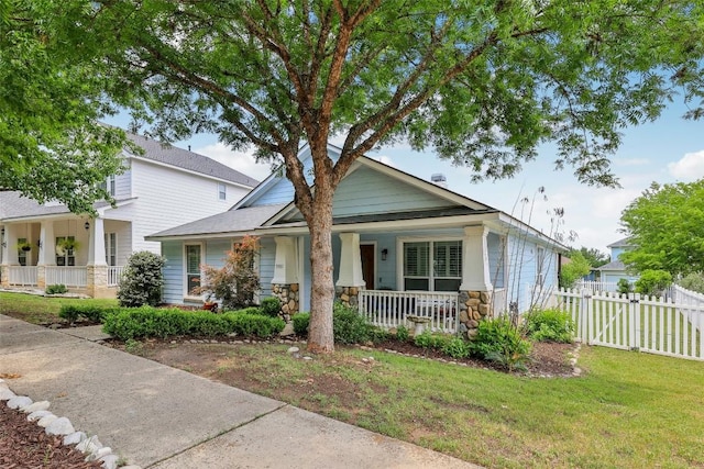 bungalow-style home with stone siding, a gate, fence, a porch, and a front lawn