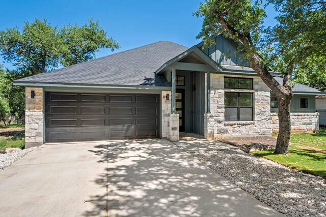 ranch-style house featuring a shingled roof, a garage, stone siding, board and batten siding, and concrete driveway