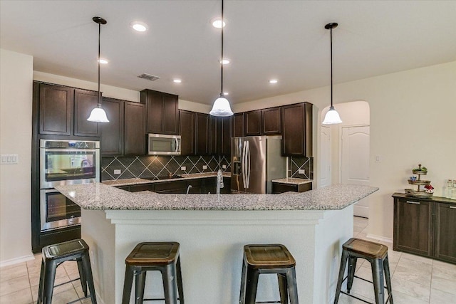 kitchen with a kitchen island with sink, stainless steel appliances, tasteful backsplash, dark brown cabinetry, and visible vents