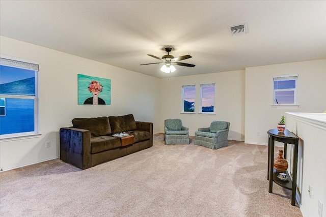living area with baseboards, visible vents, light carpet, and ceiling fan