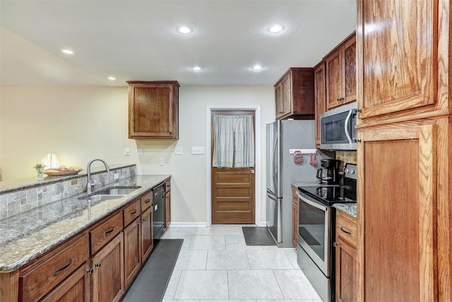kitchen featuring light stone counters, a sink, stainless steel appliances, recessed lighting, and a peninsula
