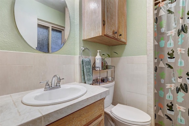 bathroom with a shower with curtain, tile walls, vanity, toilet, and a textured wall