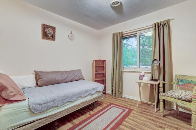 bedroom with a textured ceiling, visible vents, light wood-style flooring, and baseboards