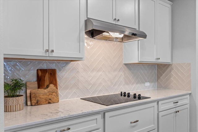 kitchen with light stone countertops, black electric stovetop, under cabinet range hood, backsplash, and white cabinetry