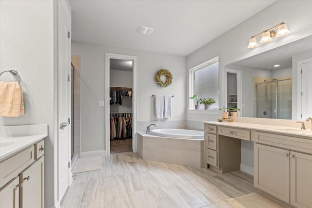 full bath with a sink, a stall shower, two vanities, a garden tub, and a spacious closet