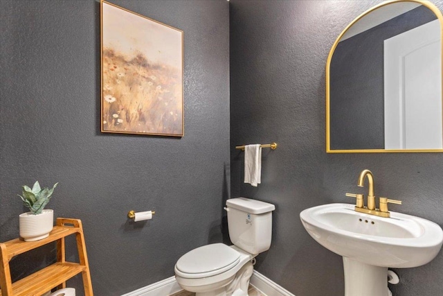 half bath with toilet, a sink, and baseboards