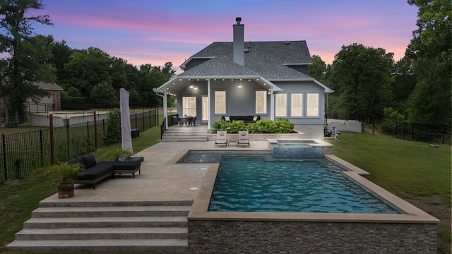 back of property at dusk with a patio area, a yard, a fenced backyard, a chimney, and stucco siding