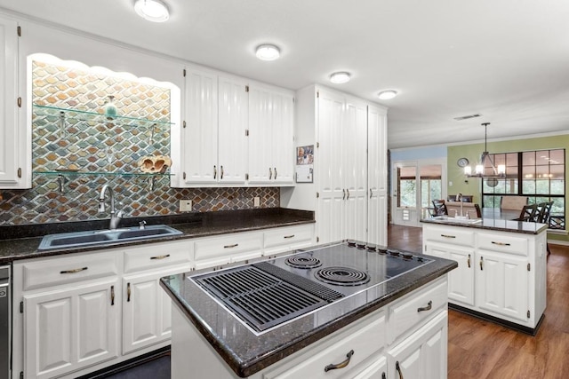 kitchen featuring black electric stovetop, a kitchen island, a sink, a notable chandelier, and dark wood-type flooring