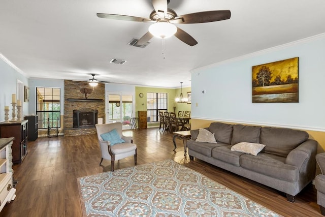 living room featuring visible vents, ceiling fan with notable chandelier, a stone fireplace, and crown molding