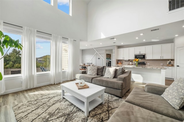 living area with visible vents, recessed lighting, light wood finished floors, and a high ceiling