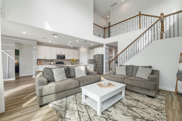 living area featuring visible vents, light wood-type flooring, recessed lighting, a towering ceiling, and stairs