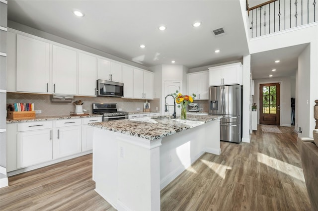 kitchen with appliances with stainless steel finishes, visible vents, tasteful backsplash, and light wood finished floors