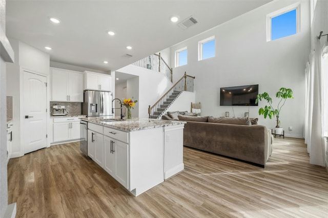 kitchen with light wood-style flooring, light stone counters, appliances with stainless steel finishes, a sink, and white cabinetry