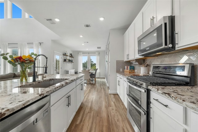kitchen with light wood-style flooring, appliances with stainless steel finishes, backsplash, a sink, and visible vents