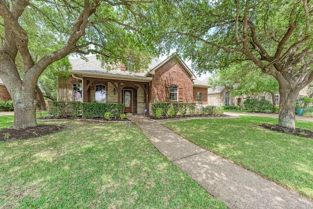 view of front of property featuring a chimney, brick siding, and a front lawn
