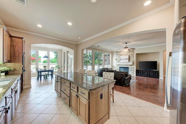 kitchen with dark stone counters, light tile patterned floors, a center island, arched walkways, and a ceiling fan