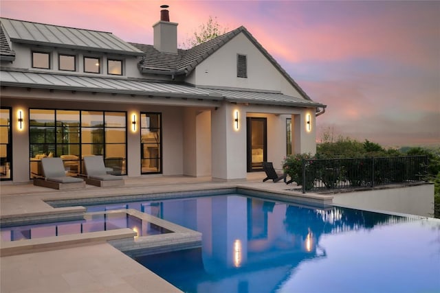 back of property at dusk featuring stucco siding, a standing seam roof, metal roof, and a patio area