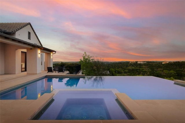 pool at dusk featuring a pool with connected hot tub and a patio area