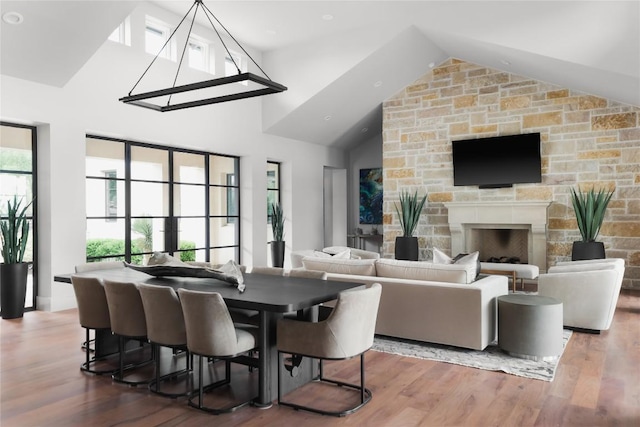 dining area featuring wood finished floors, a stone fireplace, and vaulted ceiling
