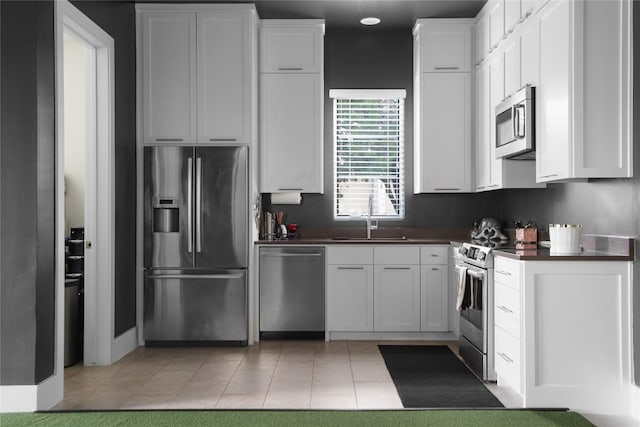 kitchen featuring a sink, light tile patterned floors, dark countertops, white cabinets, and appliances with stainless steel finishes