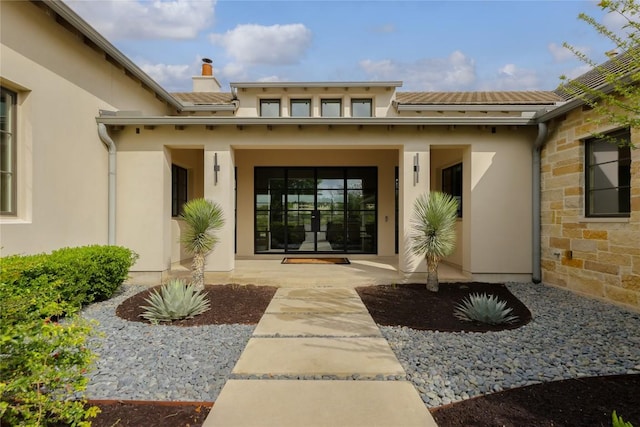 entrance to property featuring stone siding, a tile roof, a chimney, stucco siding, and a porch