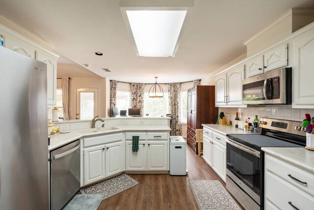 4906 Thunderbird Dr, Lago Vista, TX 78645 - kitchen featuring appliances with stainless steel finishes, a peninsula, dark wood-type flooring, tasteful backsplash, and white cabinetry