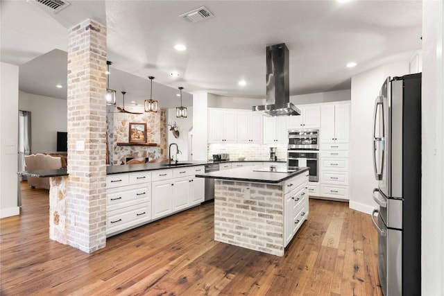 kitchen featuring decorative columns, dark countertops, appliances with stainless steel finishes, and island exhaust hood