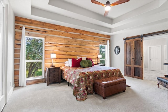 bedroom with a barn door, a raised ceiling, multiple windows, and carpet flooring