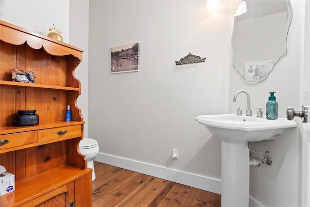 half bathroom featuring wood finished floors, toilet, and baseboards