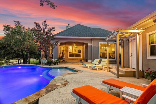 back of house at dusk featuring a patio, an outdoor pool, roof with shingles, a pergola, and stucco siding