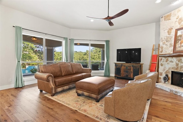 living room with ceiling fan, a stone fireplace, hardwood / wood-style flooring, and plenty of natural light