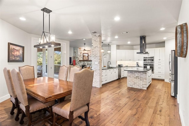 dining space featuring light wood finished floors, recessed lighting, a stone fireplace, and visible vents