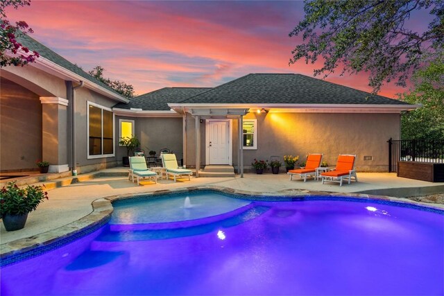 rear view of property with a patio, a shingled roof, stucco siding, and a fenced in pool