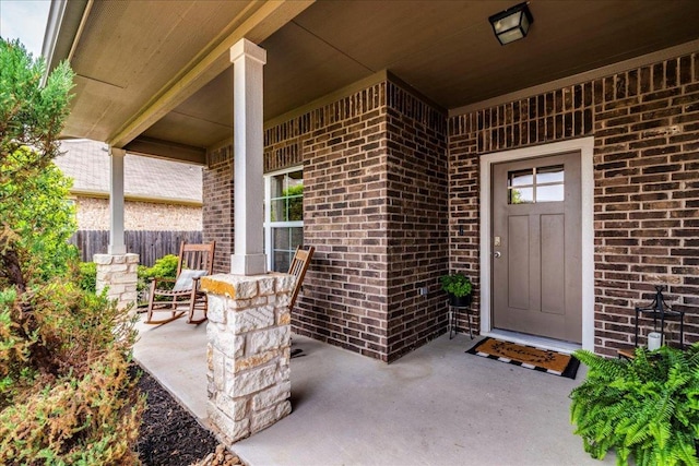 doorway to property with a porch, fence, and brick siding