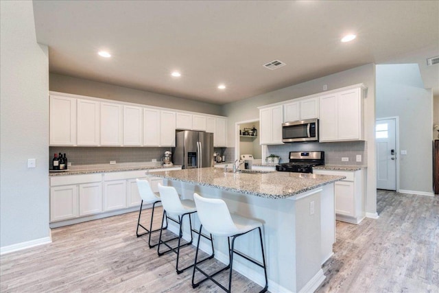 kitchen featuring a sink, stainless steel appliances, a center island with sink, visible vents, and backsplash