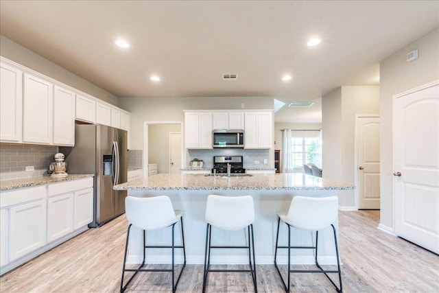 kitchen with white cabinetry, stainless steel appliances, backsplash, and light wood-style floors